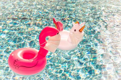 Swimming pool toys unicorn and flamingo in a medical face mask. Concept of Coronavirus outbreak impact on a travel industry for summer season 2020