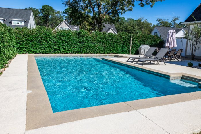 A rectangular new swimming pool with tan concrete edges in the fenced backyard of a new construction in VA, DC and MD