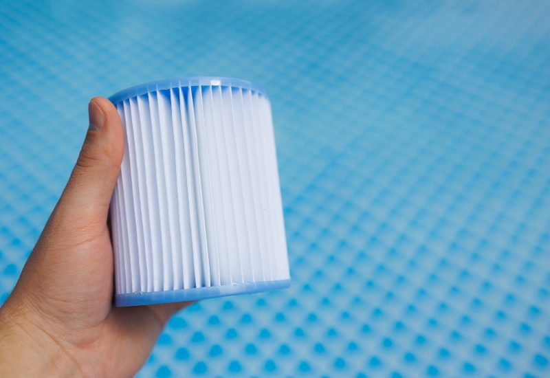 Hand holding pool filter cartridge over blue pool surface in Virginia & Maryland