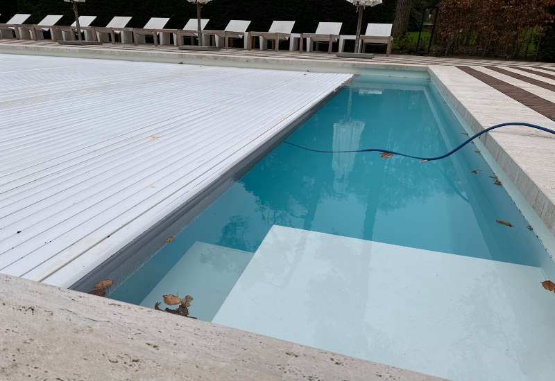 Swimming pool with retractable cover partially closed and hose in water in Virginia & Maryland