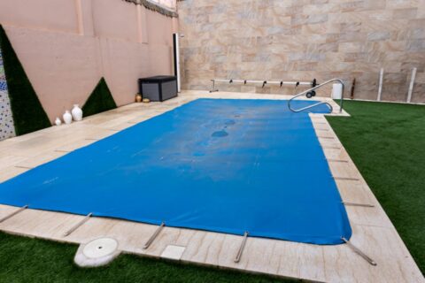 Blue safety cover secured over in-ground pool during winter closing process