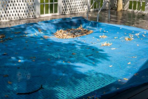 Pool covered for winter with leaves and debris collected on top of safety cover