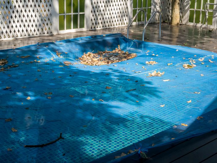 Pool covered for winter with leaves and debris collected on top of safety cover