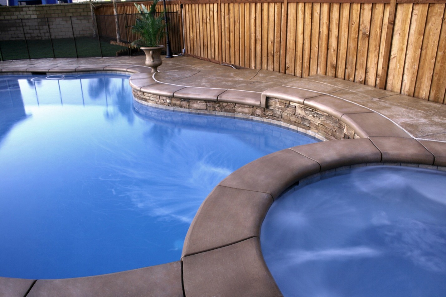 Custom backyard swimming pool with raised spa, stamped concrete deck and stone coping