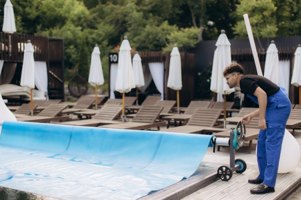 Pool technician operating pool cover roller beside outdoor swimming pool