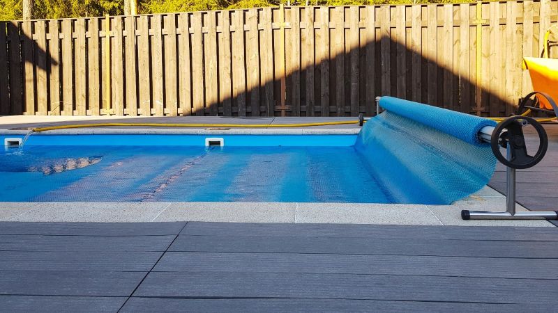 Swimming pool with blue roller cover beside a backyard deck
